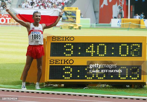 Robert Korzeniowski of Poland waves the Polish flag next to the time board, which shows his winning time and the former world record in the men's...