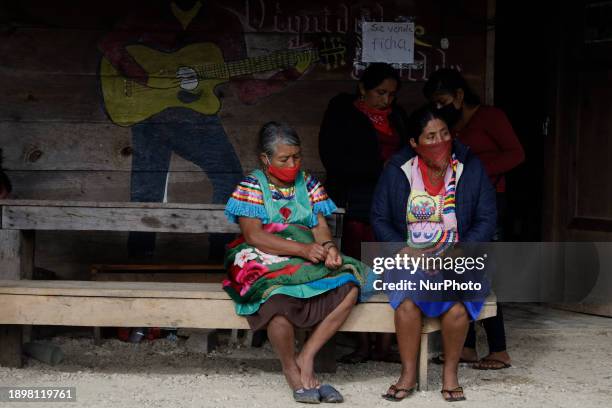 Women from the Zapatista Army of National Liberation community are sitting on a bench in El Caracol Rebeldia y Resistencia in the mountains of...