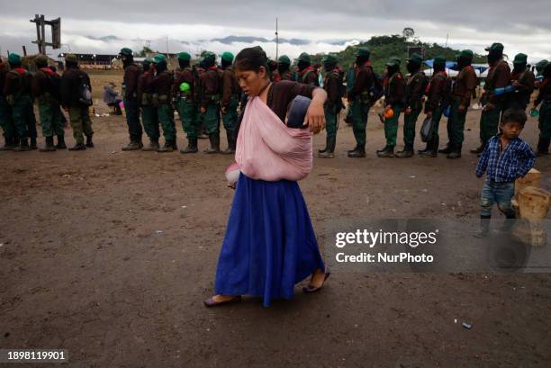 Woman is carrying a child and walking in front of members of the Zapatista Army of National Liberation in El Caracol Rebeldia y Resistencia in the...