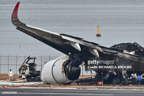 This photo taken on January 3, 2024 shows officials looking at the burnt wreckage of a Japan Airlines passenger plane on the tarmac at Tokyo...
