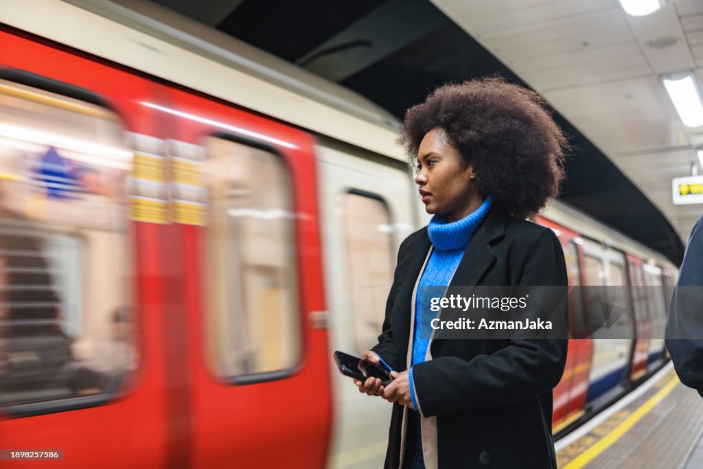 Una atractiva mujer negra adulta esperando un tren en la estación de metro de Londres