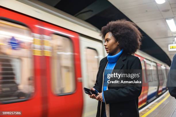 an attractive adult black female waiting for a train at the underground station in london - metro de londres imagens e fotografias de stock