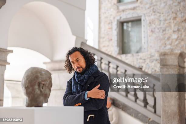 adult black male history enthusiast admiring the statue in a museum with his arms crossed - criticus stock pictures, royalty-free photos & images