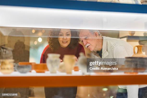 adult woman and a senior caucasian man looking at pottery vessels in a museum - art and craft show stock pictures, royalty-free photos & images