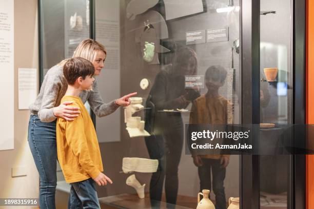 une mère caucasienne montre des artefacts à son fils et l’éduque sur l’histoire pendant qu’ils visitent un musée d’histoire - musée historique photos et images de collection
