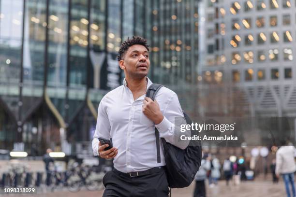 portrait of a mixed race man looking up while walking at a business district holding his cellphone - top 40 stock pictures, royalty-free photos & images