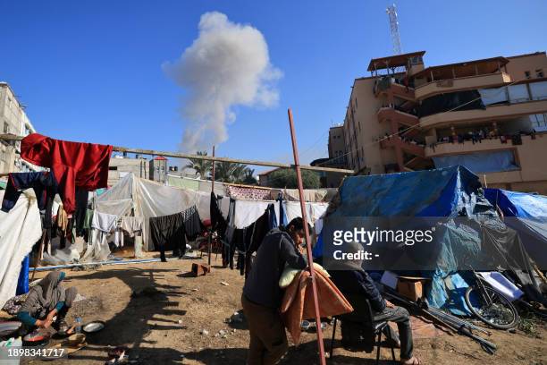 People gather near tents used as temporary shelter, as smoke rises during an Israeli strike on Khan Yunis in the southern Gaza Strip on January 4...