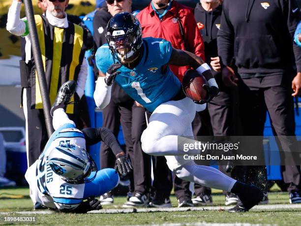 Runningback Travis Etienne Jr. #1 of the Jacksonville Jaguars makes a catch and run over Safety Xavier Woods of the Carolina Panthers during the game...