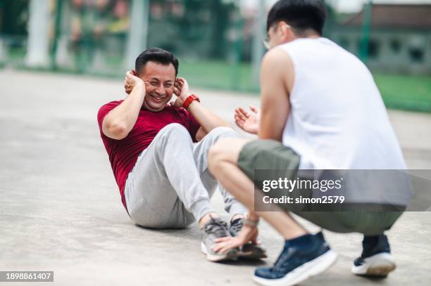 fitness drive: trainer encouraging asian man's park sit-up workout - trainer stockfoto's en -beelden