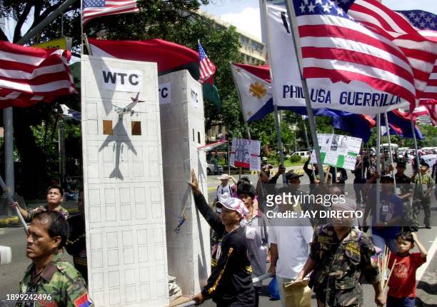 Group of Filipino demonstrators waving US flags and carrying a mock World Trade Center with a toy plane crashing on the building march to the US...