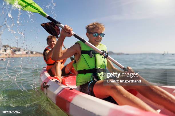 teenage kids enjoying kayaking in lyme regis on summer day - canoeing uk stock pictures, royalty-free photos & images