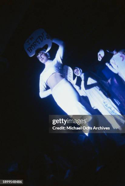 Fashion models wearing white outfits embellished with graffiti, holding speech bubbles by their heads, and bandages wrapped around their jaws, on the...