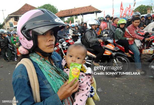 Woman waits with her child as hundreds of people on motorcycles arrive at the ferry terminal in Gilimanuk port, on the island of Bali to catch a...