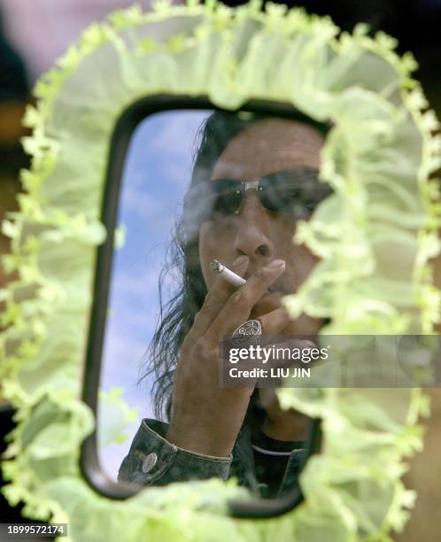 Tibetan motorbike rider is reflected in a wing mirror as he smokes during the annual Litang Horse Racing Festival in the wild west Tibetan county of...