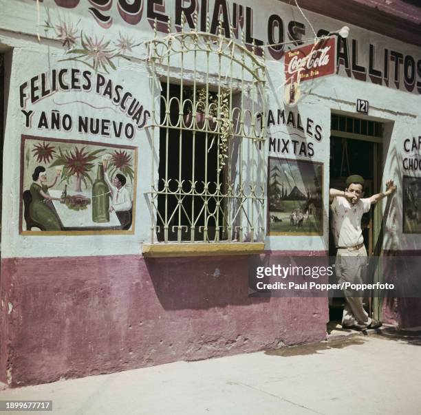 Man stands in the doorway entrance to a cafe and bar on a street in Guatemala City, capital of Guatemala in Central America, circa 1960.