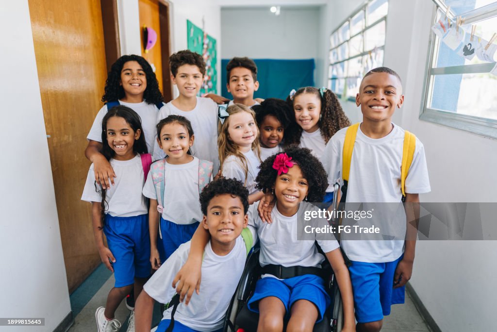 Retrato de uma menina usando cadeira de rodas com seus amigos no corredor da escola