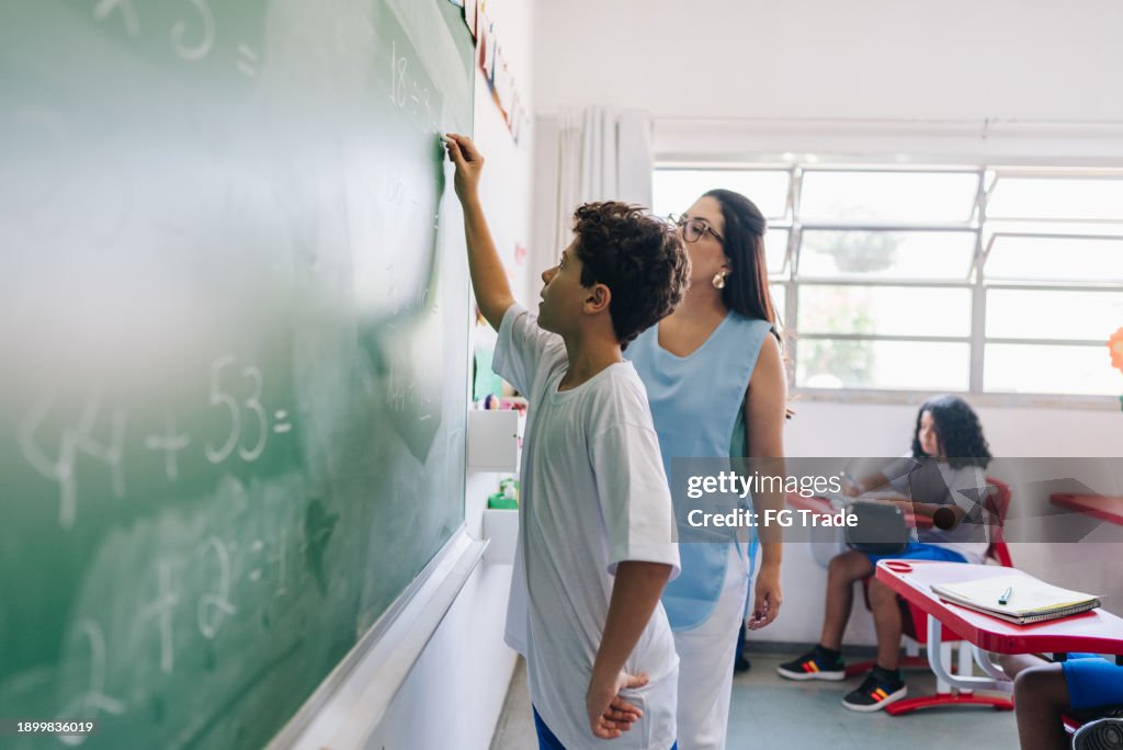 Student boy writing on chalkboard in classroom at school