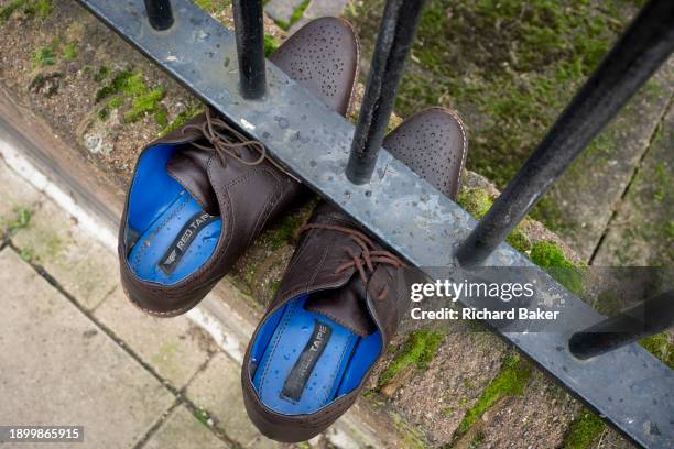 Pair of laced-up, discarded brown shoes are pinned beneath railings in a street at Loughborough Junction, on 3rd January 2024, in London, England.