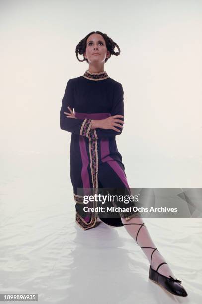 Fashion model wearing a black dress with purple trim, golden cuffs and detail and an embroidered floral pattern, and black shoes with black straps...