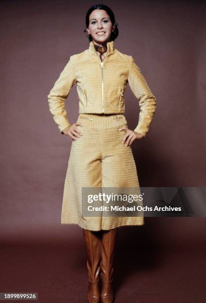 Fashion model wearing a gold-coloured trouser suit with wide-leg pedal pushers and brown boots, during a studio fashion shoot, against a brown...