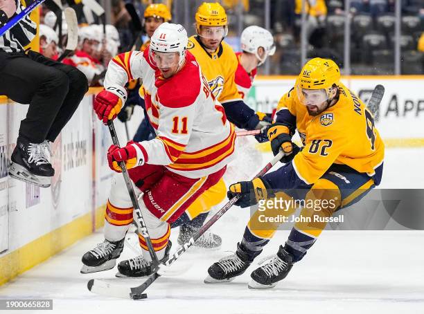 Tommy Novak of the Nashville Predators battles for the puck against Mikael Backlund of the Calgary Flames during an NHL game at Bridgestone Arena on...