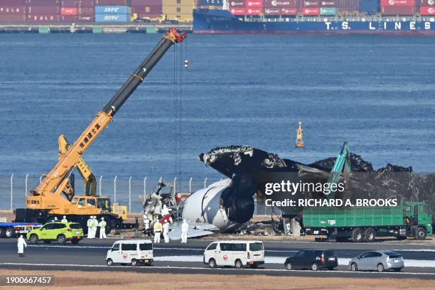 Officials remove the remaining debris of a Japan Airlines passenger plane from the runway area at Tokyo International Airport at Haneda on January 5...