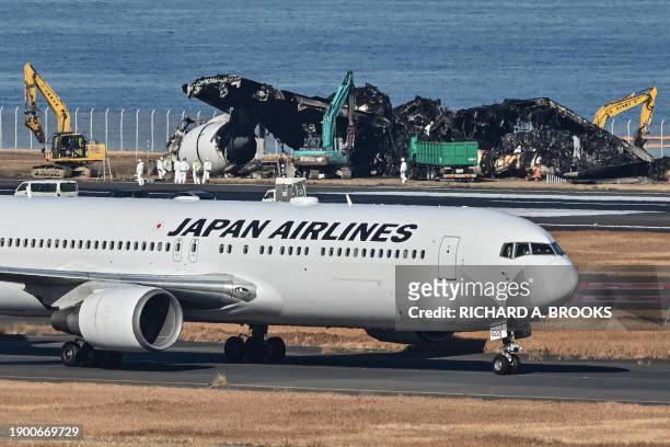 Japan Airlines plane taxis past as officials remove the remaining debris of a JAL passenger plane from the runway area at Tokyo International Airport...