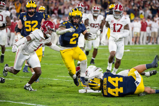 Blake Corum of the Michigan Wolverines runs with the ball for yardage away from Terrion Arnold and Kool-Aid McKinstry of the Alabama Crimson Tide...