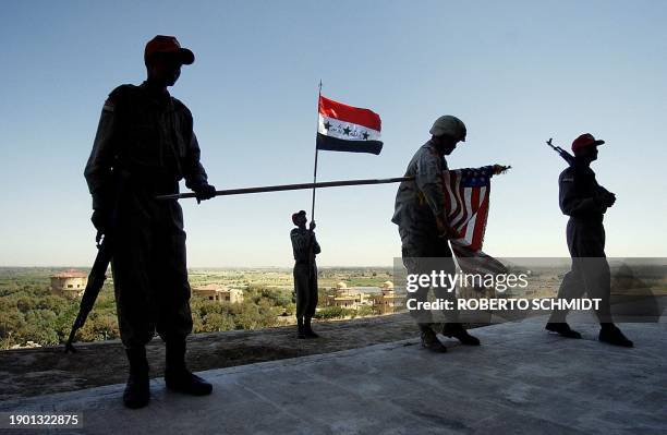 Member of the Iraqi Civil Defense Corps holds high the Iraqi flag as two of his classmates flank a US soldier unfurling a US flag outside a palace of...