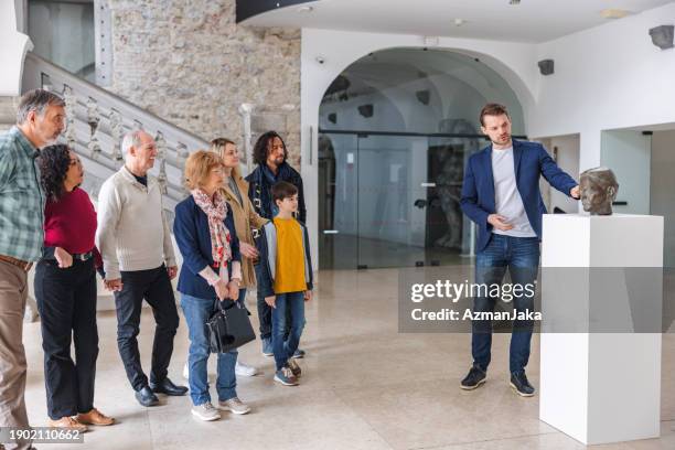 eine gruppe verschiedener museumsbesucher hört einem kaukasischen männlichen museumsführer zu, der die geschichte hinter der statue erklärt - museumswärter stock-fotos und bilder