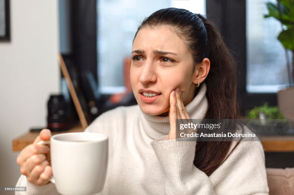 Woman drinking coffee feeling tooth pain from teeth sensitivity