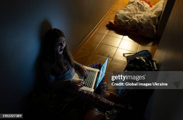 Girl sits with a laptop in the corridor of an apartment hiding during a Russian missile attack on January 2, 2024 in Kyiv, Ukraine.