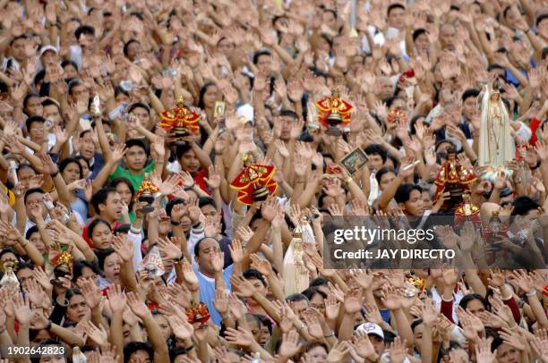 Devotees, attending a mass, raise their hands in prayer as they hold a religious icon of the Santo Niño, at the Basilica Del Santo Niño in Cebu city,...