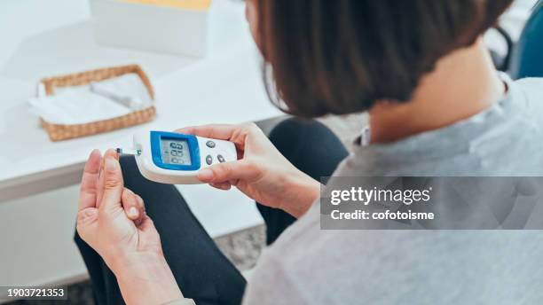mujer adulta joven que realiza un análisis de sangre de glucosa en casa - diabetes fotografías e imágenes de stock