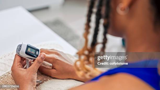 young adult woman checking oxygen saturation level at home - pulse oximeter stockfoto's en -beelden