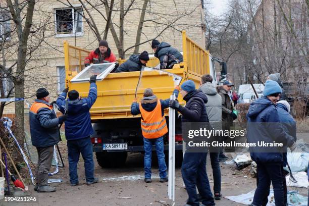 People clear debris in a yard of a residential building hit by Russian shelling in the south-western suburb of Kyiv on January 2, 2024 in Vyshneve,...