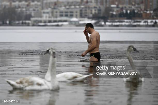 Believer makes the sign of the cross as he plunges into the waters of Dnieper river during the Epiphany celebrations in Kyiv, on January 6 amid the...
