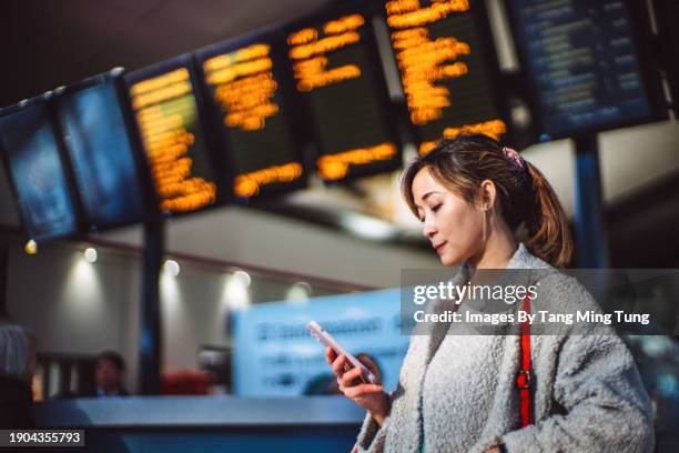 beautiful asian businesswoman using smartphone against arrival departure board at train station - ringing phone stock pictures, royalty-free photos & images