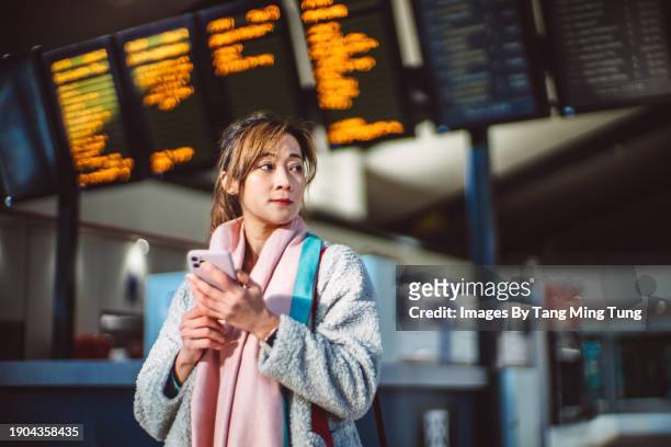 beautiful asian businesswoman using smart phone against arrival departure board at train station - one mid adult woman only stock pictures, royalty-free photos & images
