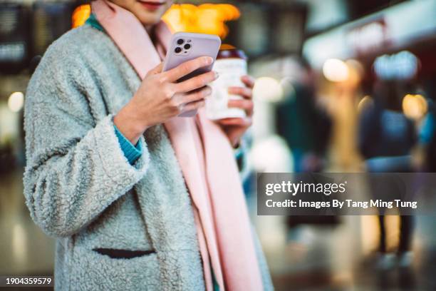 beautiful asian businesswoman with a takeaway coffee cup using smartphone against arrival departure board at train station - food and drink sign stock pictures, royalty-free photos & images