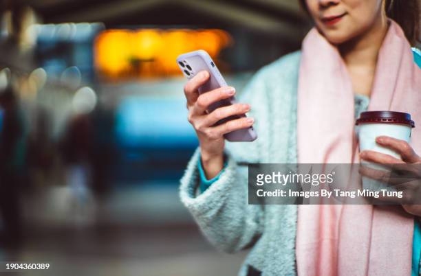 beautiful asian businesswoman with a takeaway coffee cup using smartphone against arrival departure board at train station - food and drink sign stock pictures, royalty-free photos & images