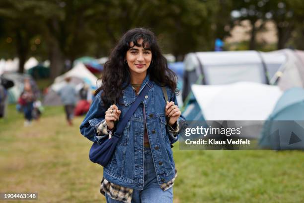 smiling woman in denim jacket walking against tents - one mid adult woman only stock pictures, royalty-free photos & images