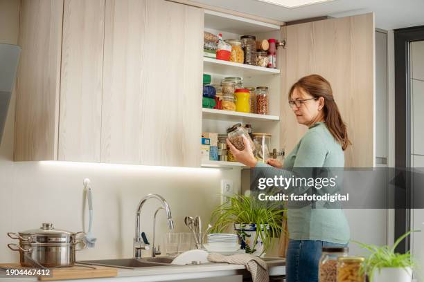 donna matura che sceglie generi alimentari in piedi davanti alla dispensa della cucina - dispensa foto e immagini stock