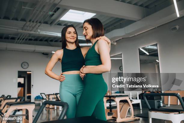 photo of two beautiful sportswomen in matching green tank tops and leggings standing in spacious gym with several pilates reformer machines - promises rehab center foto e immagini stock