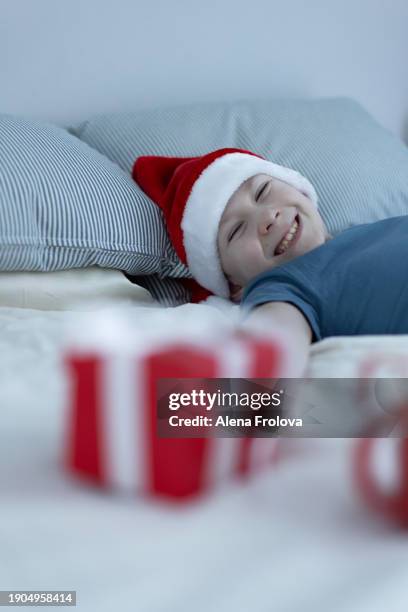 a boy in santa hat  lies on a bed on white linens and plays with a christmas tree toy holding cup christmas - big country breakfast stock pictures, royalty-free photos & images