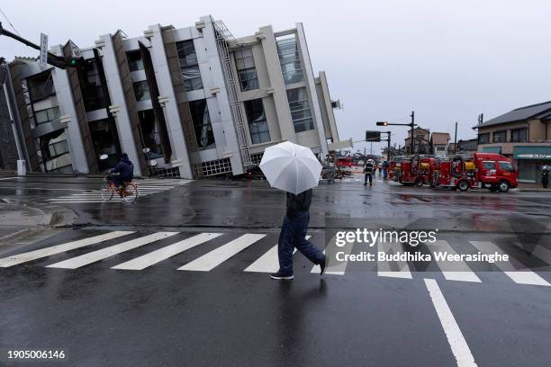 Man crosses the road in front of a collapsed building on January 03, 2024 in Wajima, Japan. A series of major earthquakes have killed more than 60...