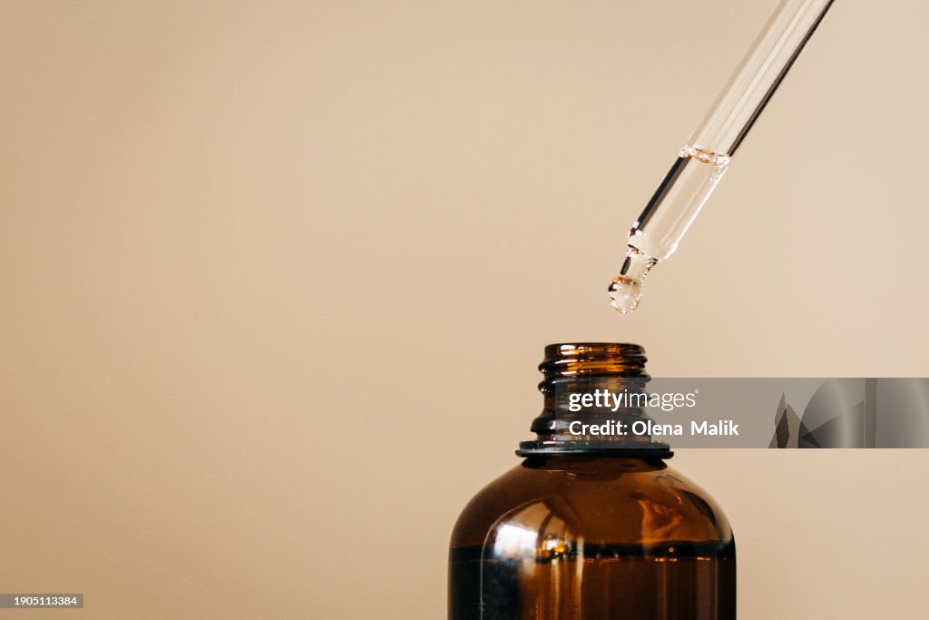 Close up of face serum pouring from a pipette into an amber glass bottle. Natural skincare and essential oil aromatherapy. Health and wellness concept. Copy space.