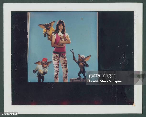 Portrait of American actress Phoebe Cates as she poses with several creatures, two 'gremlins' and on a 'mogwai' , from the film 'Gremlins' , as she...