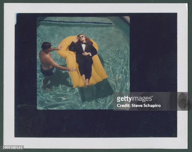 An unidentified man stands in a pool and holds an inflatable chair on which reclines American actress Diane Lane, barefoot and dressed in a suit and...