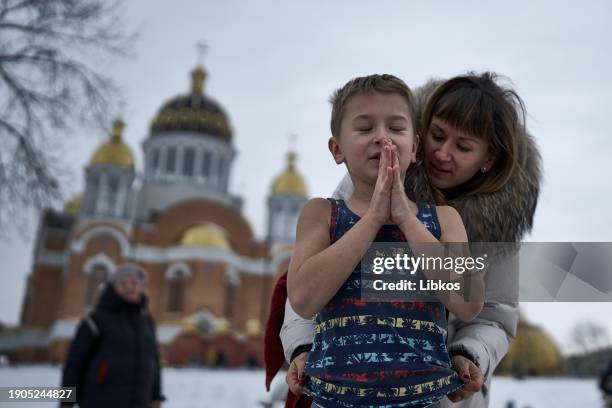 Mother prepares a child for immersion against the background of a church as Ukrainians perform the rite of immersion in icy water during Epiphany...